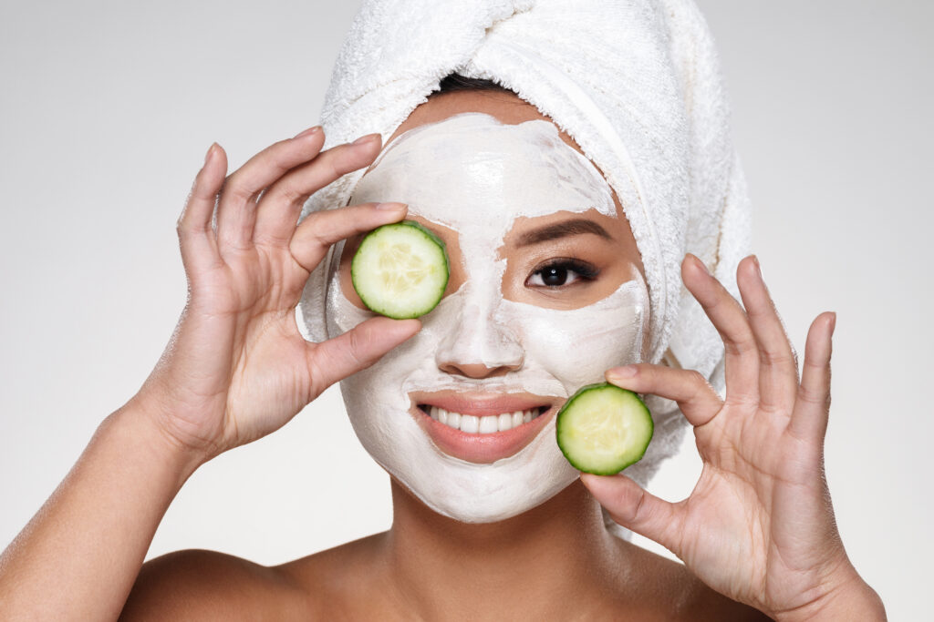 attractive smiling lady with scrab on face holding cucumber slices isolated